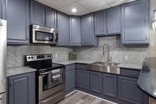 kitchen with a drop ceiling, a sink, appliances with stainless steel finishes, light wood finished floors, and tasteful backsplash