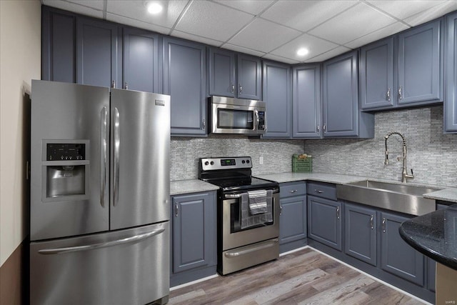 kitchen with light wood-style flooring, decorative backsplash, appliances with stainless steel finishes, a sink, and light stone countertops