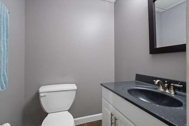 half bath with baseboards, vanity, and toilet