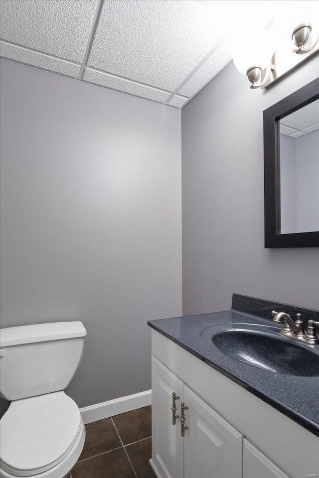 half bath featuring baseboards, toilet, tile patterned flooring, vanity, and a paneled ceiling