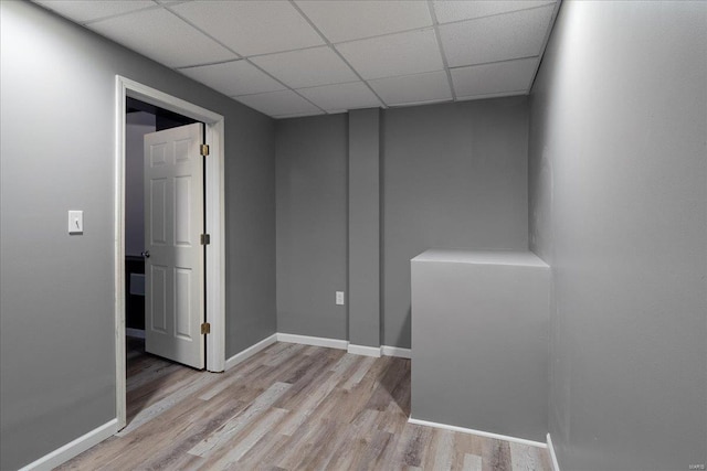 empty room featuring light wood-type flooring, a paneled ceiling, and baseboards