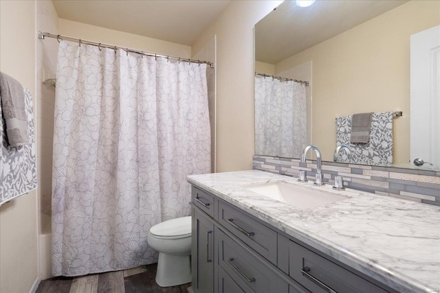 full bath featuring toilet, wood finished floors, vanity, shower / tub combo with curtain, and tasteful backsplash