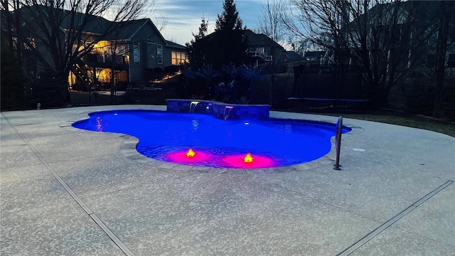 pool at dusk with a trampoline, a patio area, and an outdoor pool