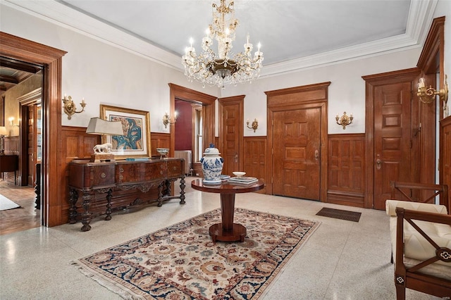 entryway with a notable chandelier, crown molding, and wainscoting