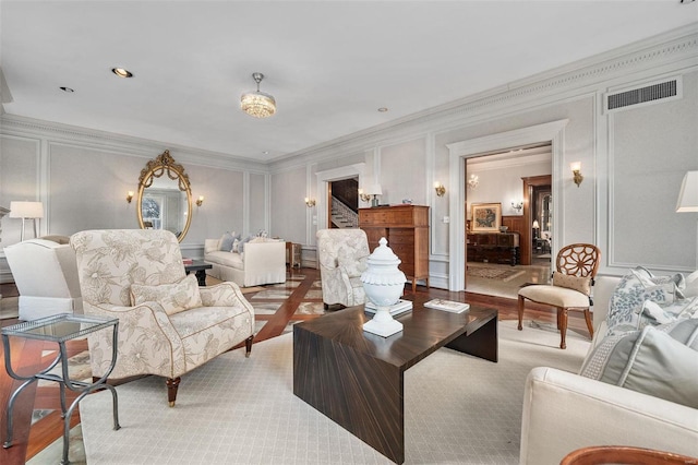 living area featuring crown molding, visible vents, a decorative wall, stairway, and wood finished floors