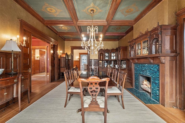 dining area with coffered ceiling, wood finished floors, an inviting chandelier, a fireplace, and beam ceiling