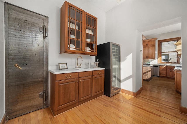 kitchen with appliances with stainless steel finishes, brown cabinetry, light wood-type flooring, and a sink