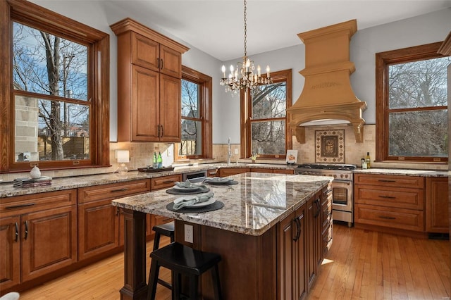 kitchen featuring a center island, custom exhaust hood, light stone countertops, light wood-type flooring, and high end range