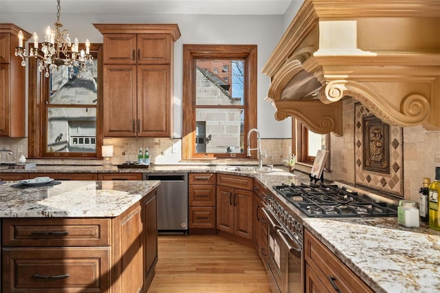 kitchen with appliances with stainless steel finishes, brown cabinets, light stone countertops, light wood-style floors, and a sink