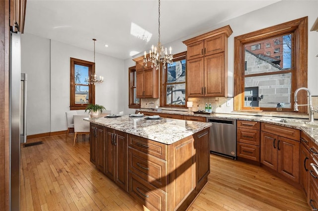 kitchen featuring backsplash, appliances with stainless steel finishes, light wood-style floors, a sink, and a chandelier