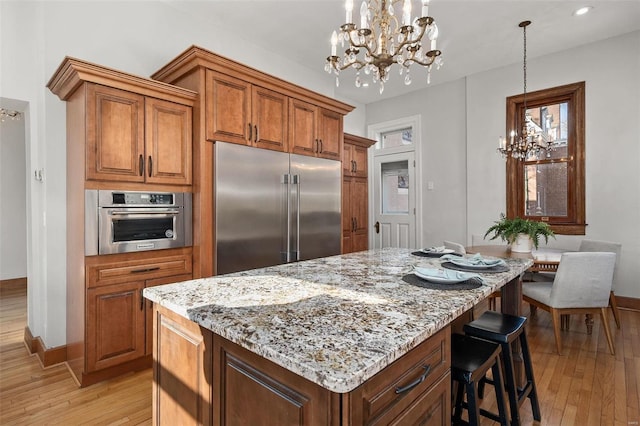 kitchen with light stone counters, stainless steel appliances, light wood-style floors, brown cabinets, and an inviting chandelier