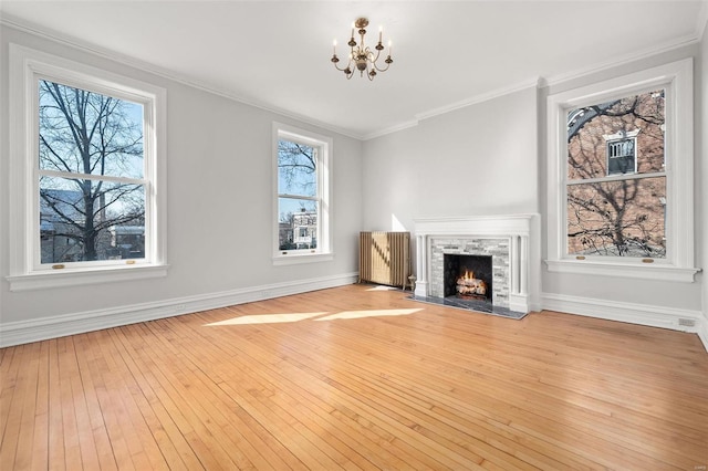 unfurnished living room with crown molding, a high end fireplace, baseboards, wood-type flooring, and an inviting chandelier