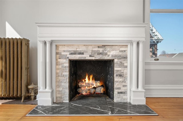 interior details with radiator heating unit, decorative columns, wood finished floors, and a fireplace with flush hearth