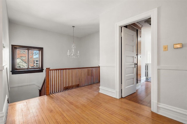 corridor featuring an inviting chandelier, wood-type flooring, baseboards, and an upstairs landing