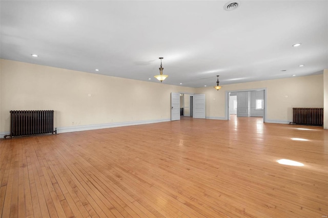 unfurnished living room with light wood-type flooring, visible vents, and radiator heating unit