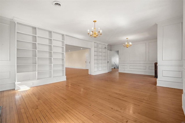 unfurnished room featuring visible vents, an inviting chandelier, light wood-style floors, built in shelves, and a decorative wall