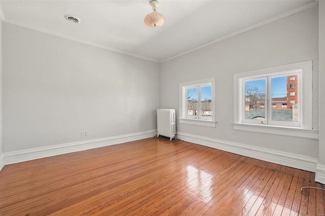 empty room with crown molding, radiator, visible vents, baseboards, and hardwood / wood-style flooring