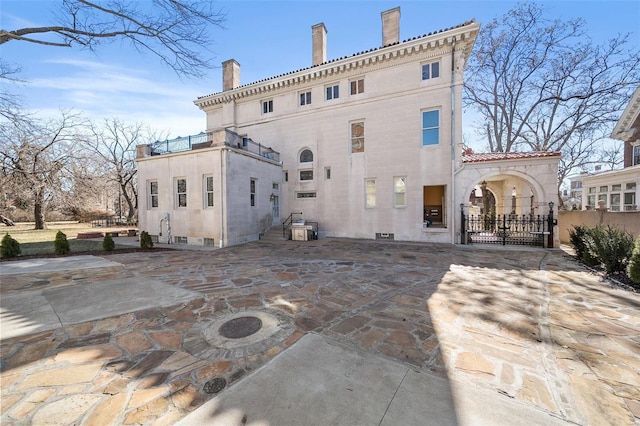 back of property with a gate, a chimney, and a patio