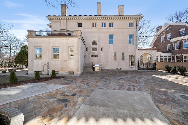 rear view of property featuring a balcony, crawl space, a gate, and a chimney