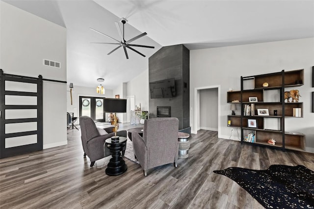 living area featuring a barn door, a tile fireplace, wood finished floors, visible vents, and a ceiling fan