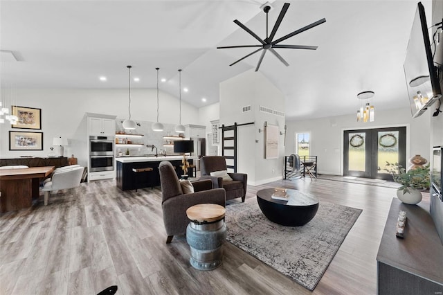 living area featuring high vaulted ceiling, a barn door, visible vents, french doors, and light wood finished floors