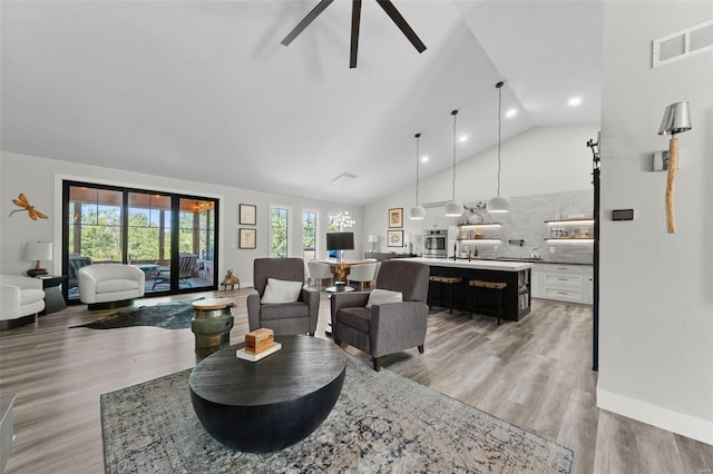 living area featuring high vaulted ceiling, light wood-type flooring, a healthy amount of sunlight, and visible vents