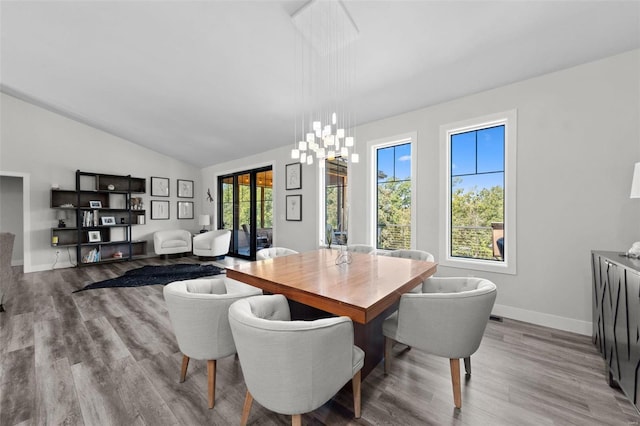 dining space with vaulted ceiling, light wood-type flooring, baseboards, and an inviting chandelier