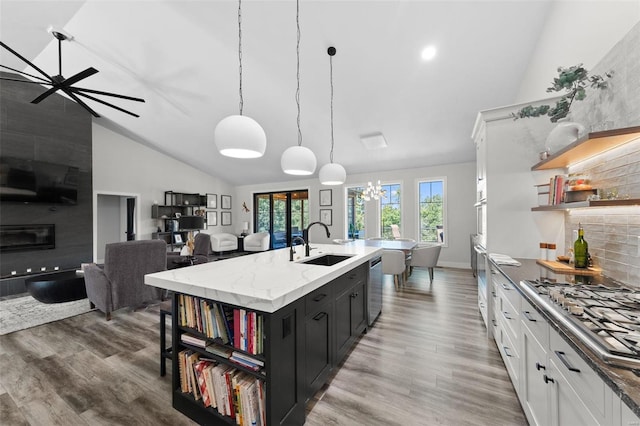 kitchen with an island with sink, dark cabinets, decorative light fixtures, white cabinetry, and a sink