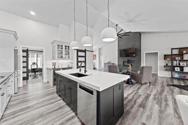 kitchen featuring white cabinets, an island with sink, open floor plan, hanging light fixtures, and stainless steel appliances