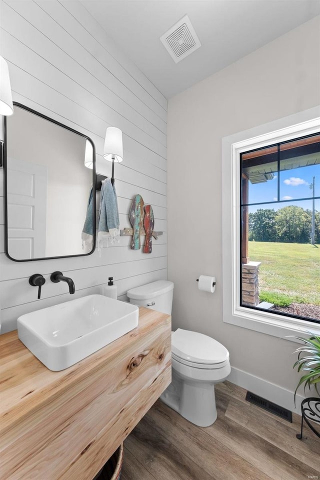 half bath with baseboards, visible vents, toilet, wood finished floors, and vanity