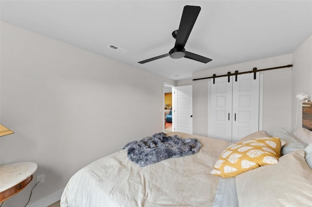 bedroom featuring a barn door, a closet, visible vents, and a ceiling fan