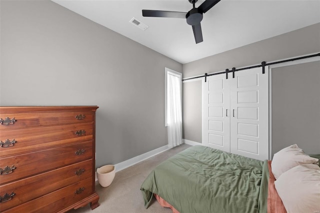 bedroom with a barn door, light colored carpet, a ceiling fan, baseboards, and visible vents