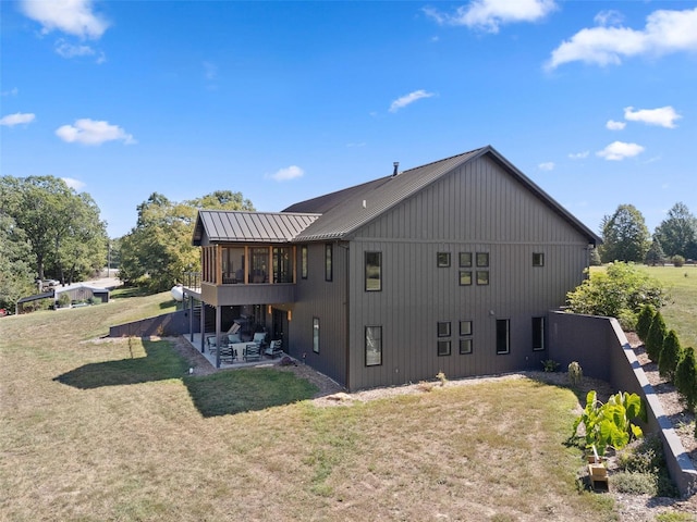 rear view of property with a yard, a patio, a standing seam roof, a sunroom, and metal roof