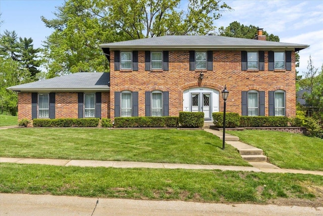 colonial house featuring brick siding, a chimney, roof with shingles, and a front lawn