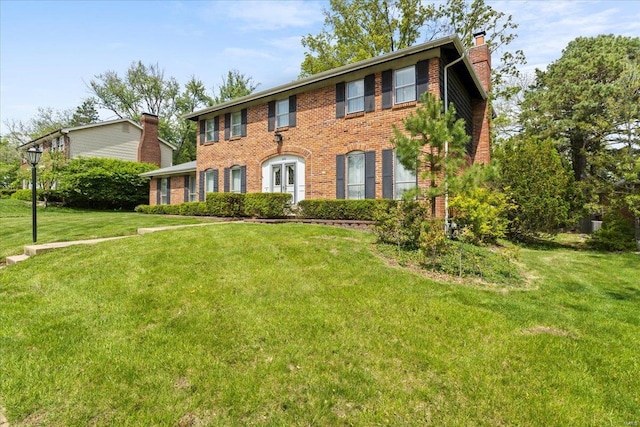 colonial home with brick siding, a front lawn, and a chimney