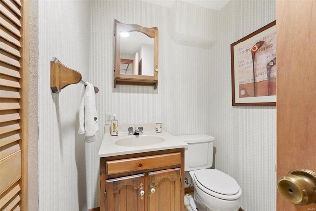 bathroom featuring toilet, wallpapered walls, and vanity