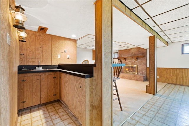 kitchen featuring wood walls, a brick fireplace, dark countertops, light floors, and a sink