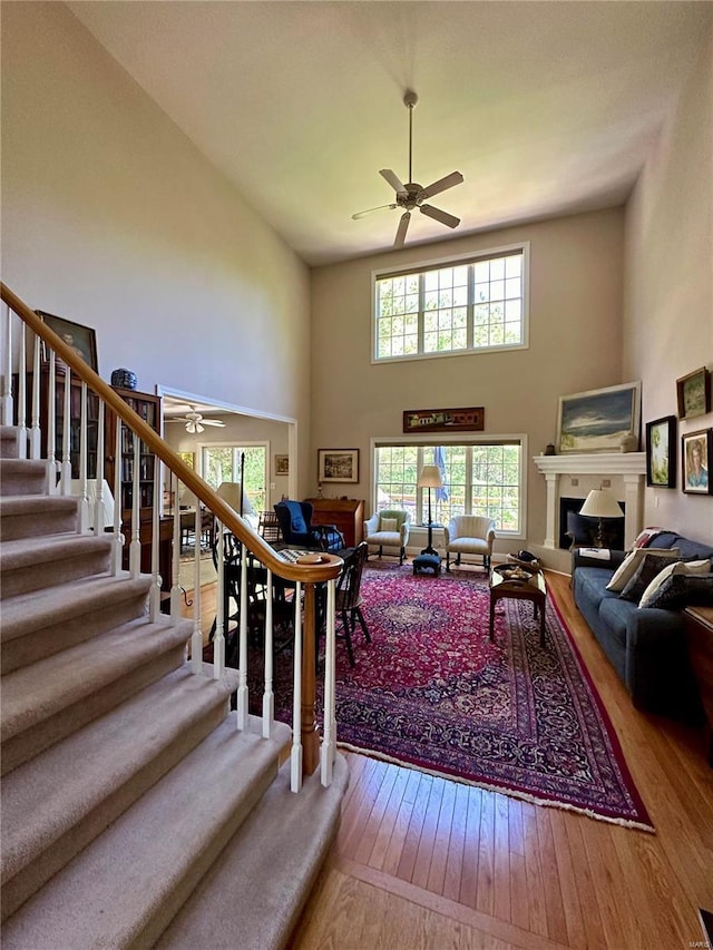 living room featuring ceiling fan, stairs, a fireplace, and wood finished floors