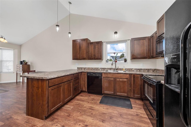 kitchen with a peninsula, light wood-type flooring, black appliances, pendant lighting, and a sink