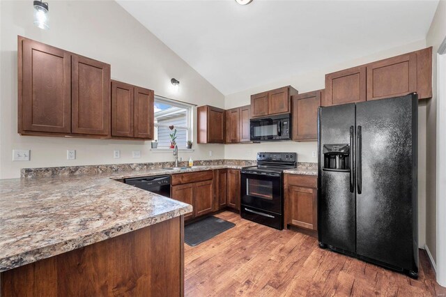 kitchen with light wood finished floors, light countertops, vaulted ceiling, black appliances, and a sink