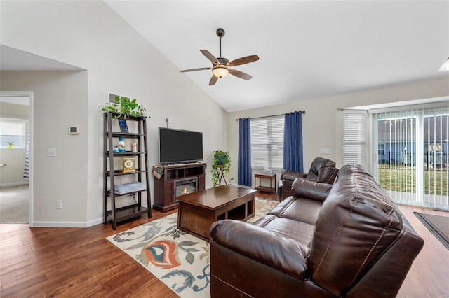 living room with ceiling fan, high vaulted ceiling, wood finished floors, baseboards, and a glass covered fireplace