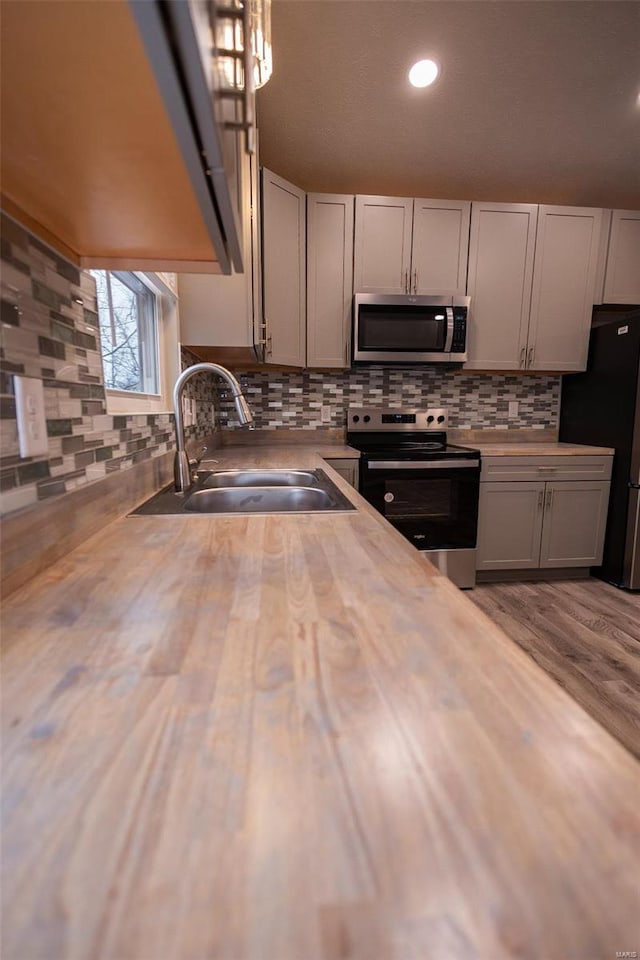 kitchen with stainless steel appliances, butcher block counters, a sink, light wood finished floors, and tasteful backsplash