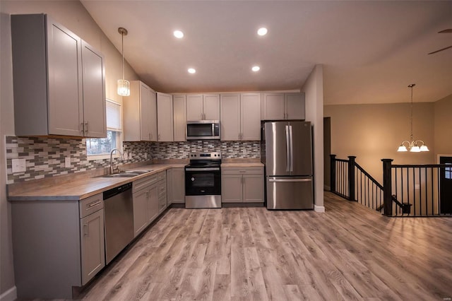 kitchen with stainless steel appliances, hanging light fixtures, a sink, and gray cabinetry