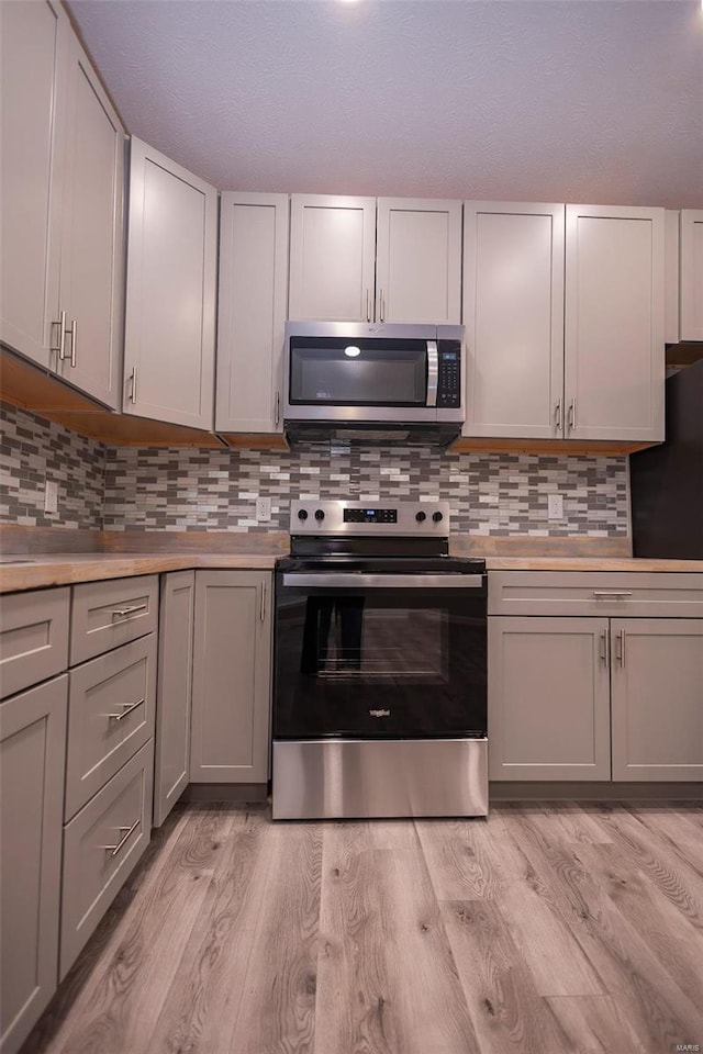 kitchen featuring stainless steel appliances, tasteful backsplash, light countertops, light wood-style flooring, and gray cabinetry