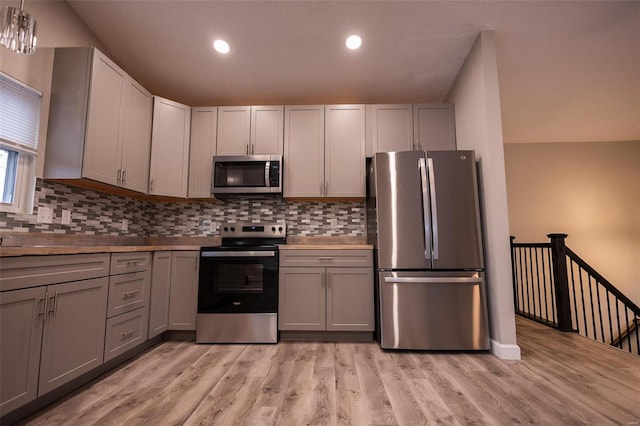 kitchen featuring light wood finished floors, gray cabinets, stainless steel appliances, light countertops, and backsplash