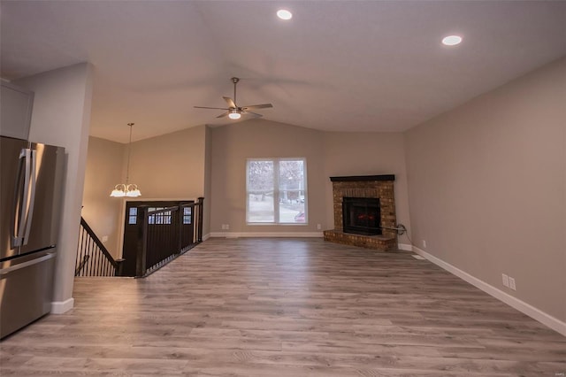 unfurnished living room featuring a brick fireplace, baseboards, vaulted ceiling, light wood-style floors, and ceiling fan with notable chandelier