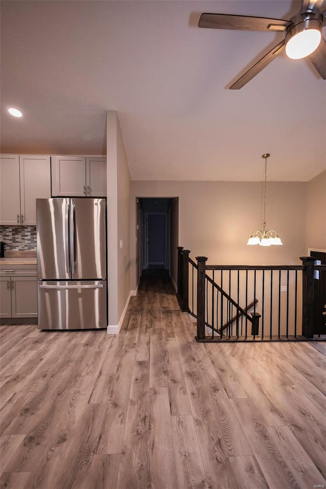 kitchen with light wood-style floors, light countertops, freestanding refrigerator, tasteful backsplash, and decorative light fixtures