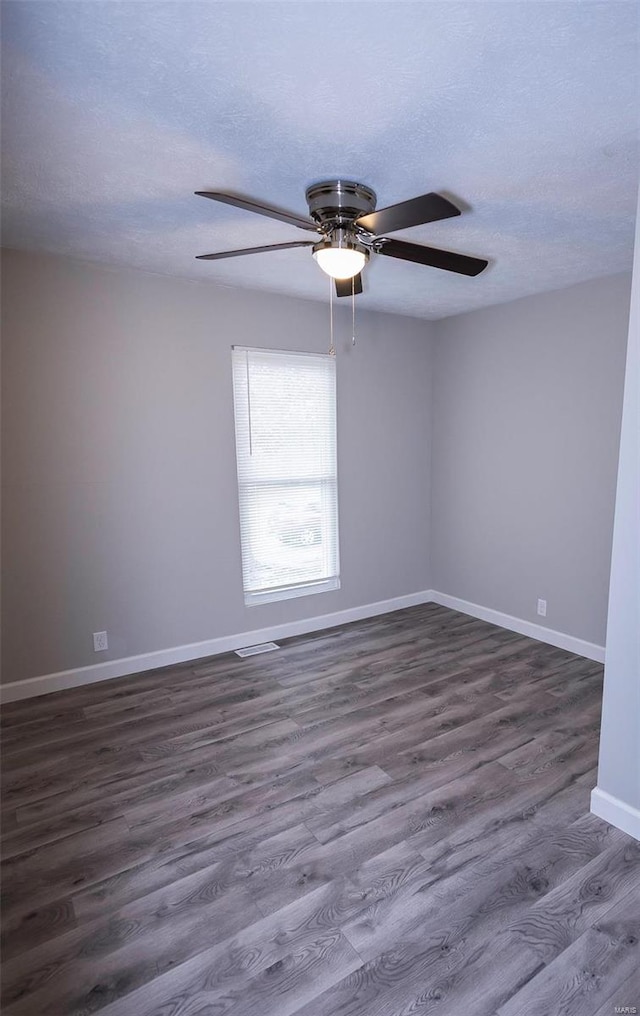 empty room with ceiling fan, a textured ceiling, baseboards, and dark wood-type flooring