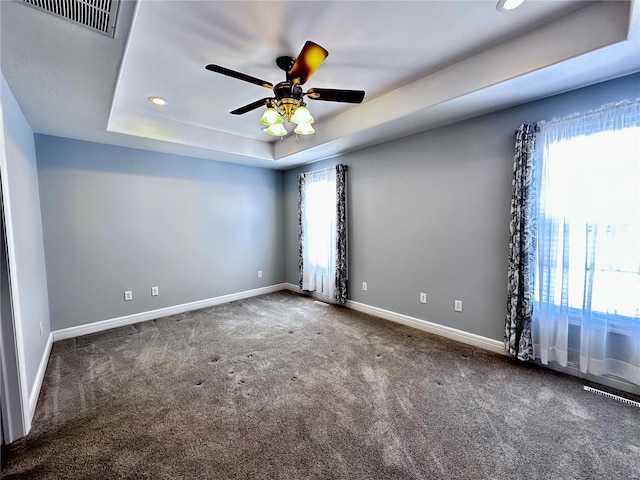 spare room featuring a ceiling fan, visible vents, baseboards, dark carpet, and a raised ceiling