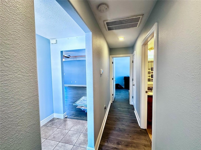 hallway with a textured wall, light wood-style floors, visible vents, and baseboards